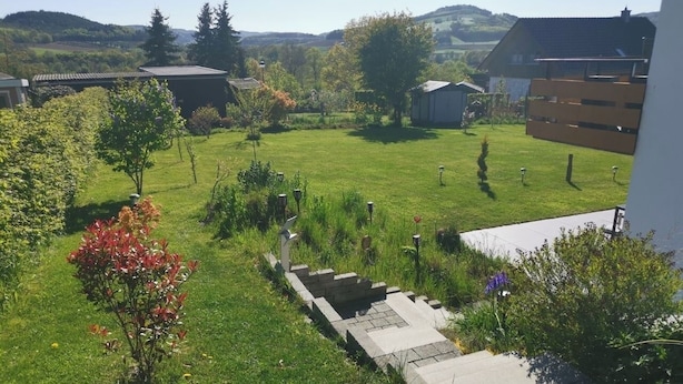 A residential area with a grassy lawn, a small garden, and a paved pathway leading to a building.