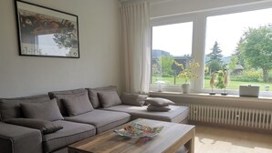 A living room with a grey sofa, a wooden coffee table, and a window with a view of greenery.