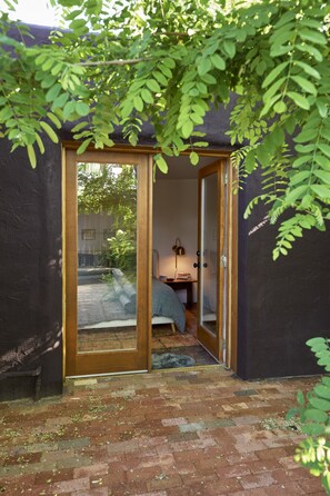 A room with a bed, a small table with a lamp, and a window overlooking a garden. - Inviting 1bd Sanctuary - The Michu Suite (Santa Fe)