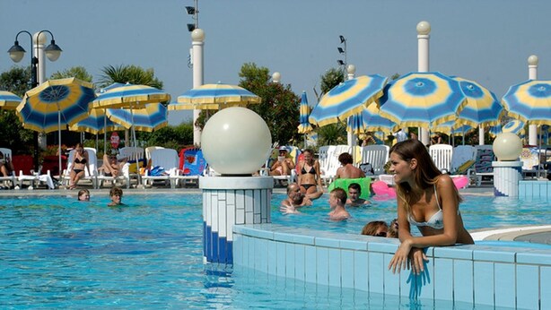 Une piscine où se trouvent plusieurs personnes, entourée de parasols et de chaises longues.