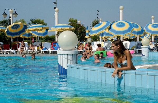 Une piscine où se trouvent plusieurs personnes, entourée de parasols et de chaises longues.