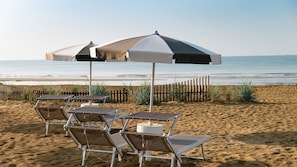 A beach with sun loungers and umbrellas, a wooden fence, and the ocean in the background. - Sun, sea and family Comfort in Bibione (Bibione)