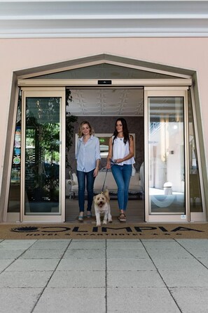 Two people standing in front of a hotel entrance with a dog on a leash.