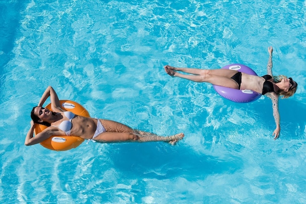 Dos personas flotando en una piscina azul cristalina con aros inflables.