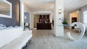 Un vestíbulo de hotel moderno con una recepción, un sofá blanco y una mesa de cristal única con una gran letra blanca 'G'.