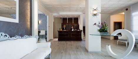 Un vestíbulo de hotel moderno con una recepción, un sofá blanco y una mesa de cristal única con una gran letra blanca 'G'.