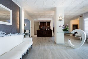 Un moderno vestíbulo de hotel con un mostrador de recepción, un sofá blanco y una mesa de vidrio única con una gran letra blanca 'G'.