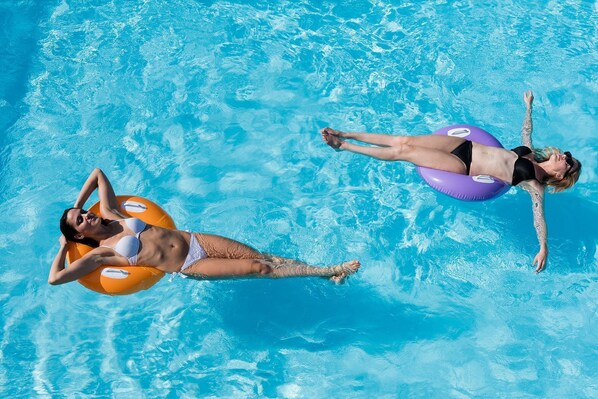 Dos personas flotando en una piscina azul cristalina con aros inflables.