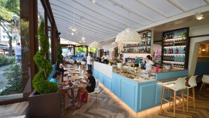 Un café interior con suelo de madera, una zona de bar con vitrina de vidrio y diferentes disposiciones de asientos.