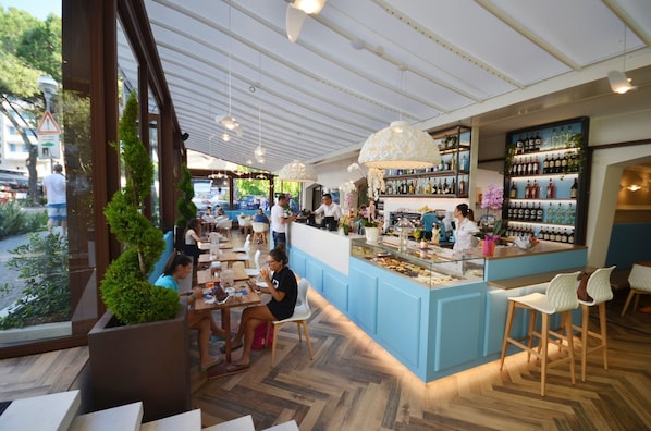 An indoor restaurant with a bar area, wooden flooring, and large windows overlooking a street. - Cozy bedroom with balcony for one in Bibione (Bibione)