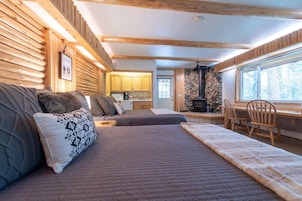 Interior acogedor de una cabaña de troncos con cama, una mesa de comedor y una zona de cocina.