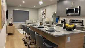 A modern kitchen with a central island, bar stools, a microwave, and a sink.