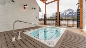 A wooden deck with a hot tub, metal railings, and a view of snow-capped mountains.