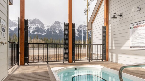 A hot tub with a mountain view, wooden deck, and a metal fence.