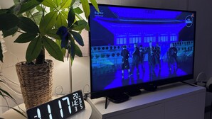 Un téléviseur diffusant une émission, une horloge numérique et une plante en pot.