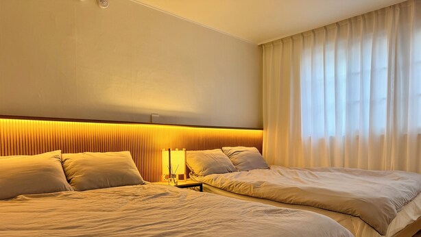 Une chambre d’hôtel avec deux lits, une table de chevet, une lampe et une fenêtre avec des rideaux.