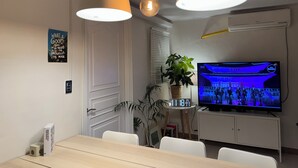 Un salon moderne avec une table à manger, des suspensions lumineuses, un téléviseur diffusant une émission et une citation inspirante sur le mur.