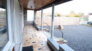 A covered outdoor area with a tiled floor, steps leading to a door, and a gravel path.