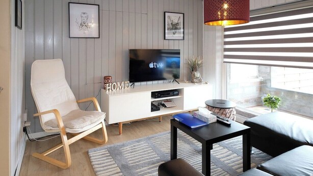 A modern living room with a flat-screen TV, a white sofa, a black coffee table, and a wooden rocking chair.
