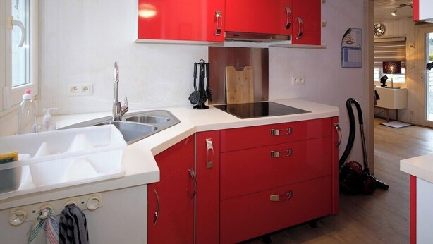 A compact kitchen with red cabinets, a white countertop, and a visible sink.