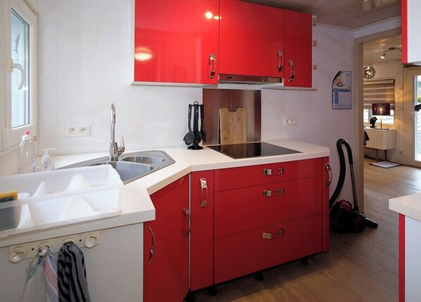 Una cocina compacta con armarios rojos, encimera blanca y un lavamanos a la vista.