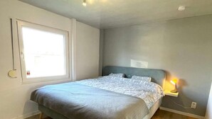 A bedroom with a bed, a window, a bedside lamp, and a wall-mounted light.