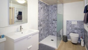 Un baño con lavamanos blanco, cabina de ducha de cristal, inodoro y baldosas estampadas.