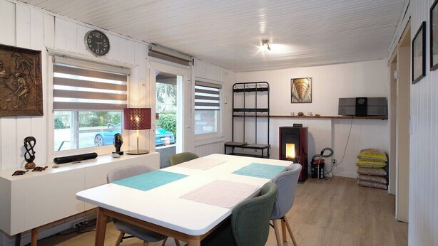 Una habitación acogedora con una mesa blanca, sillas, un reloj, una chimenea y una ventana con persianas.