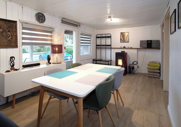 Una habitación acogedora con una mesa blanca, sillas, un reloj, una chimenea y una ventana con persianas.