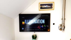 Un téléviseur à écran plat fixé au mur, au-dessus d’un meuble noir servant de support pour les appareils multimédias, et sur lequel est posée une petite plante.