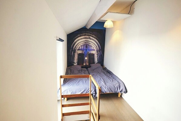 A dormitory room with two single beds, a wooden bunk bed, and a mural on the wall.