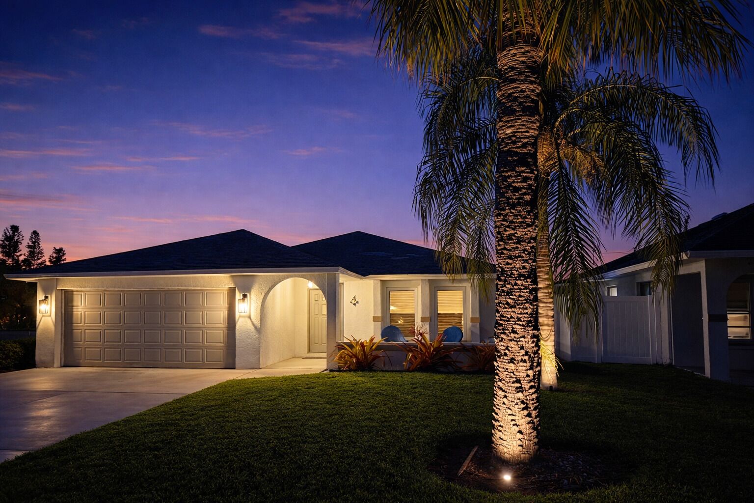 A modern house with a garage, a well-maintained lawn, and a palm tree.