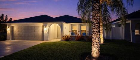 A modern house with a garage, a well-maintained lawn, and a palm tree.