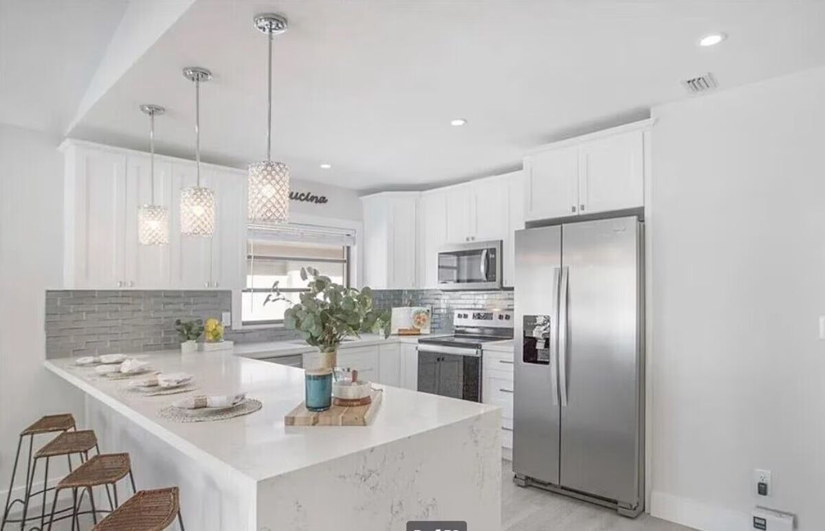 A modern kitchen with white cabinets, stainless steel appliances, and pendant lighting.