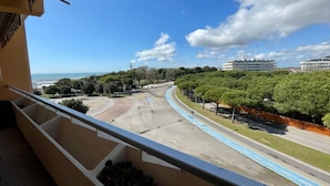 A balcony with a view of a coastal road, trees, and buildings in the distance. - Comfortable Beachfront Apartment (Caorle)