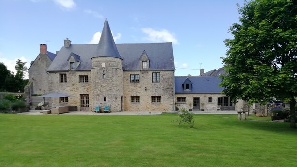 A stone building with a conical tower, a well-maintained lawn, and outdoor seating.