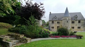 A stone building with a conical roof, surrounded by a well-maintained garden with grass and flowering plants.