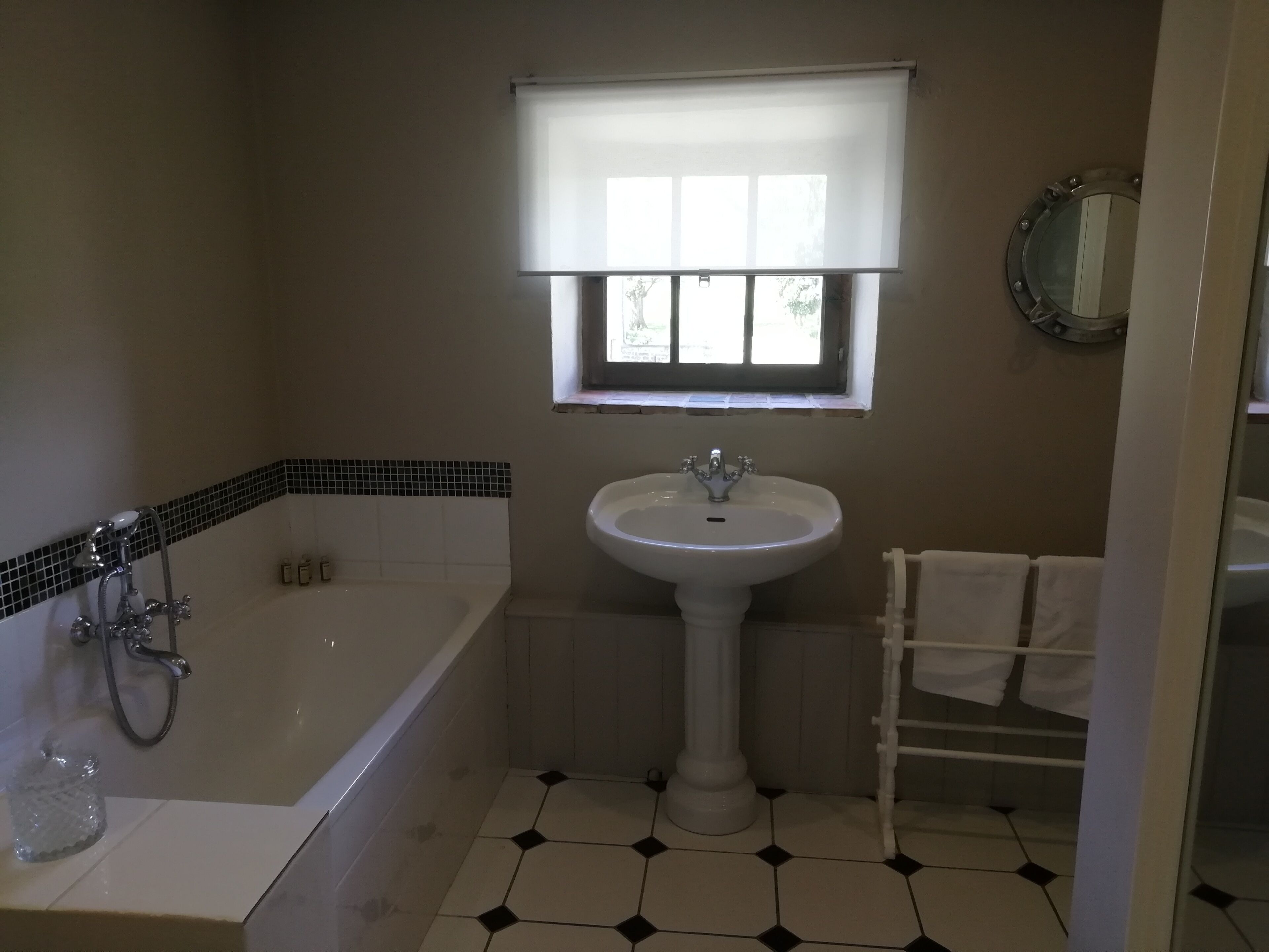 A bathroom with a bathtub, a pedestal sink, a window with blinds, and a mirror on the wall.
