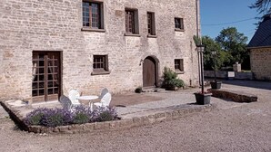 A stone building with a courtyard, featuring a door, windows, and outdoor seating.