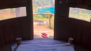 A cozy room with a bed, a view of a forest and a beach through a large window, and a wooden ceiling. - Kök Kamp (Fethiye)