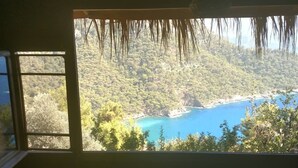 A room with a large window overlooking a forested area and a body of water. - Kök Kamp (Fethiye)