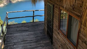 A wooden cabin with a thatched roof, a wooden deck, and a view of a lake and mountains. - Kök Kamp (Fethiye)