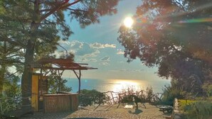 A swimming pool with a clear view of the sunset over the ocean, surrounded by a stone patio and greenery. - Kök Kamp (Fethiye)