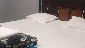 Un lit simple avec une tête de lit en bois, du linge de lit blanc et une couverture bleue.