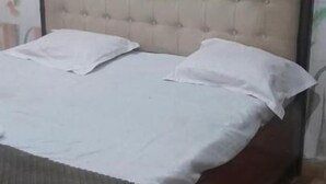 Une chambre à coucher avec une tête de lit capitonnée, un lit recouvert de draps blancs et un papier peint à motifs.