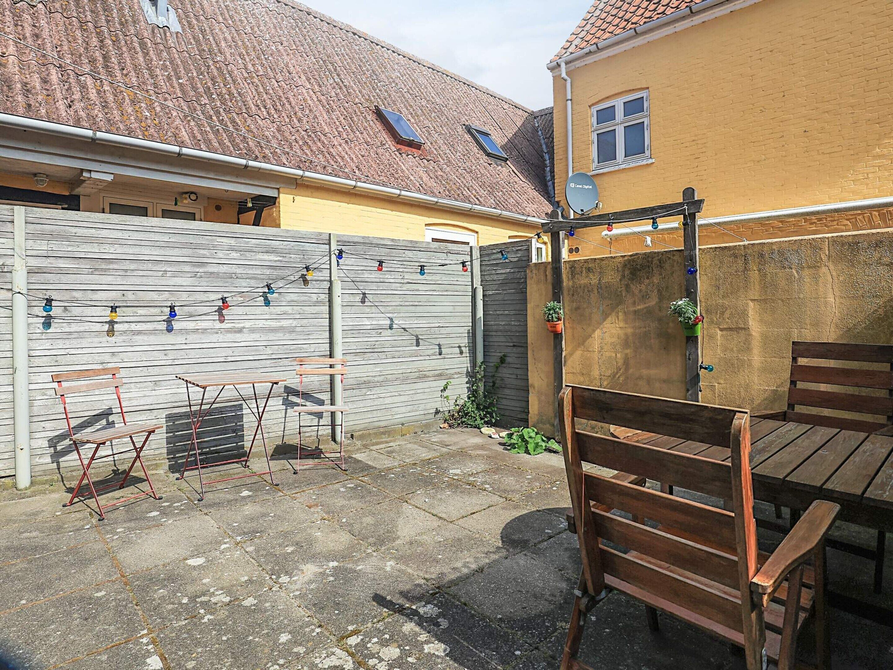 Eine Terrasse mit Tisch und Stühlen, ein Holzzaun und ein kleiner Garten.