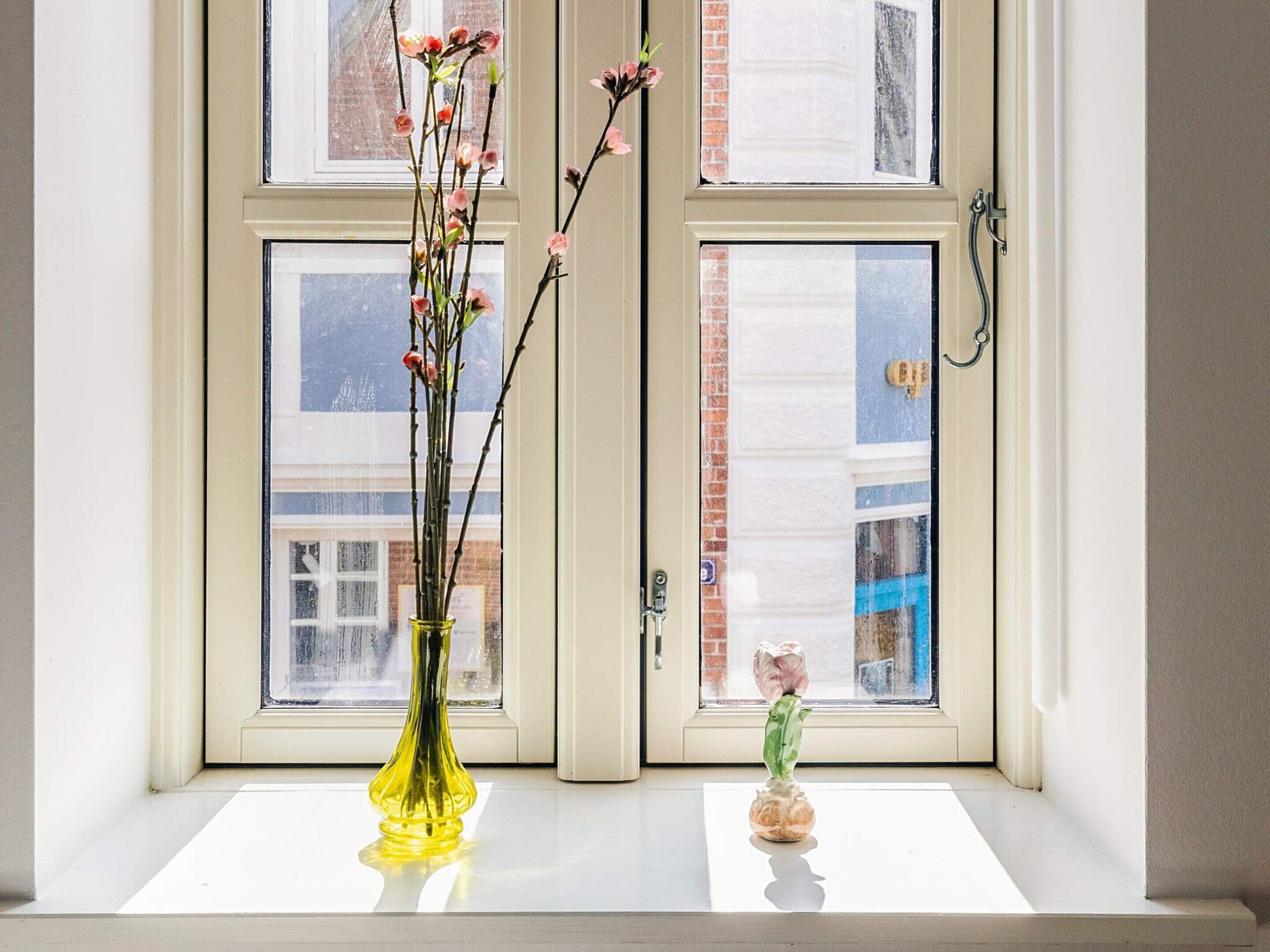 Un alféizar con dos jarrones, uno con flores rosadas y el otro con una pequeña planta.