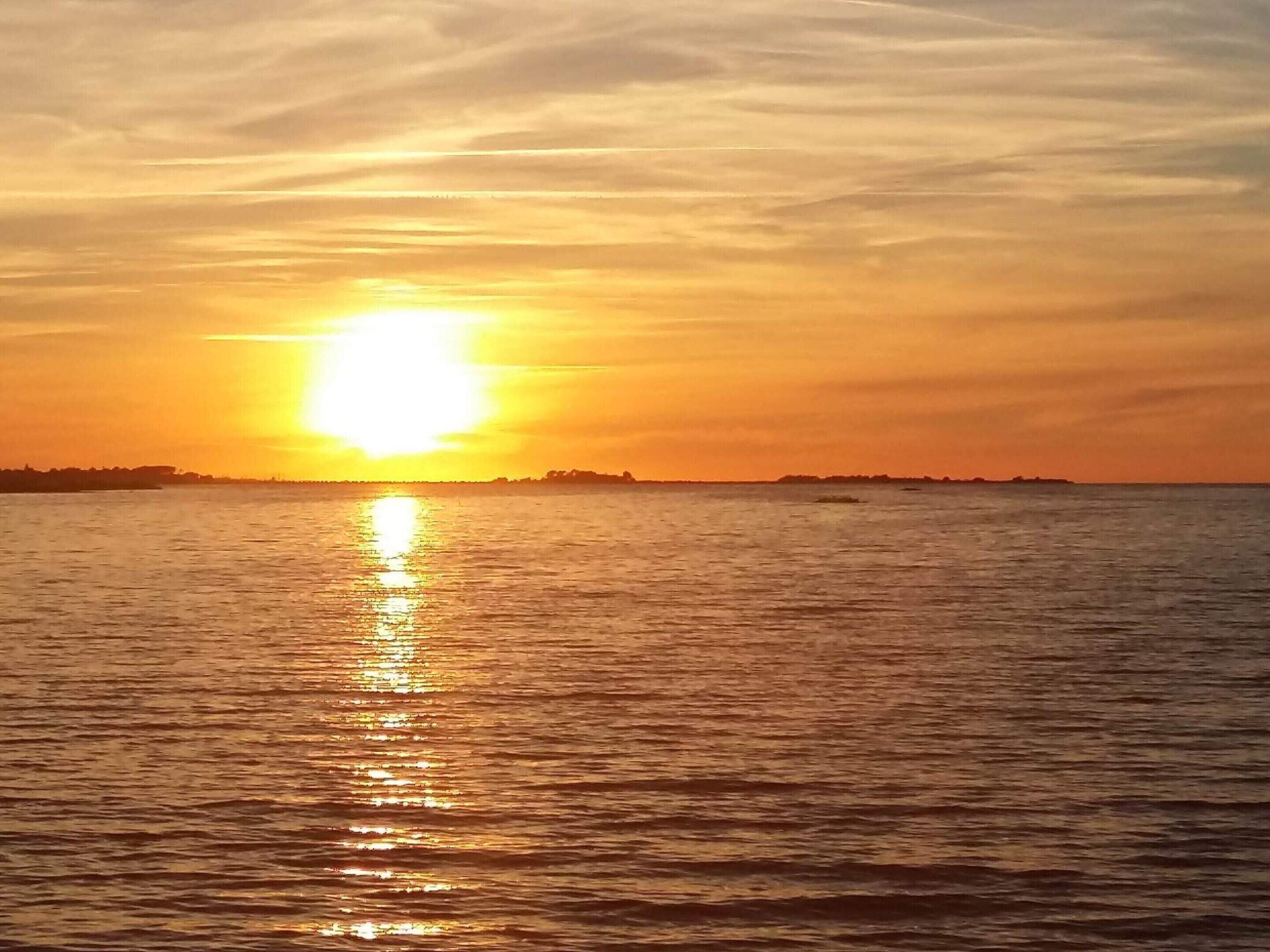A sunset over a body of water with a distant shoreline.