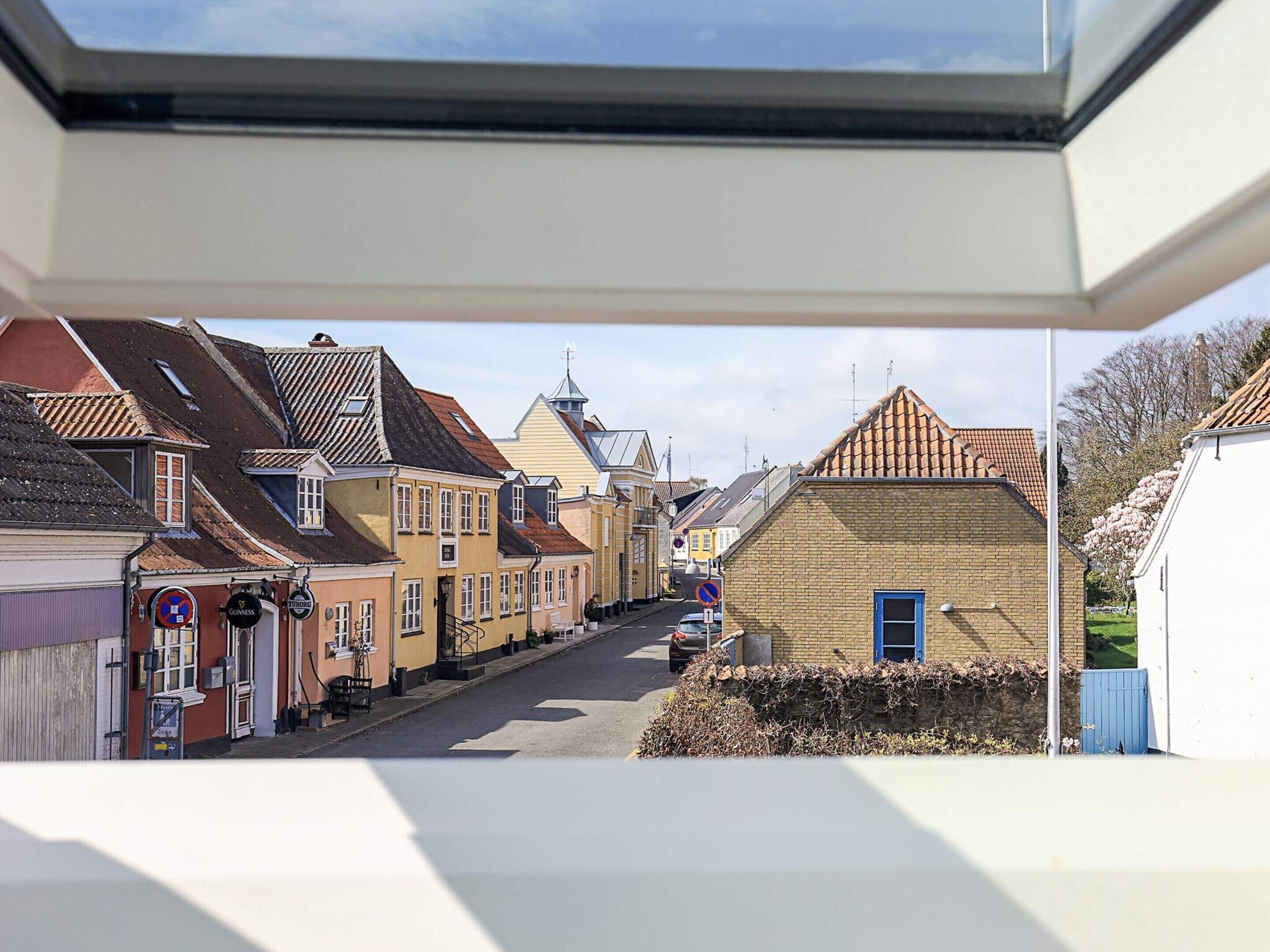 Une rue étroite bordée de bâtiments aux couleurs vives, un ciel dégagé et un ciel bleu visible à travers une lucarne.
