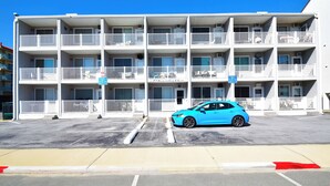 A multi-story motel with balconies, a parking lot, and a blue car parked in front. - Mirabella 1D-Oceanside 122nd St, AC, Free WiFi. (Ocean City)
